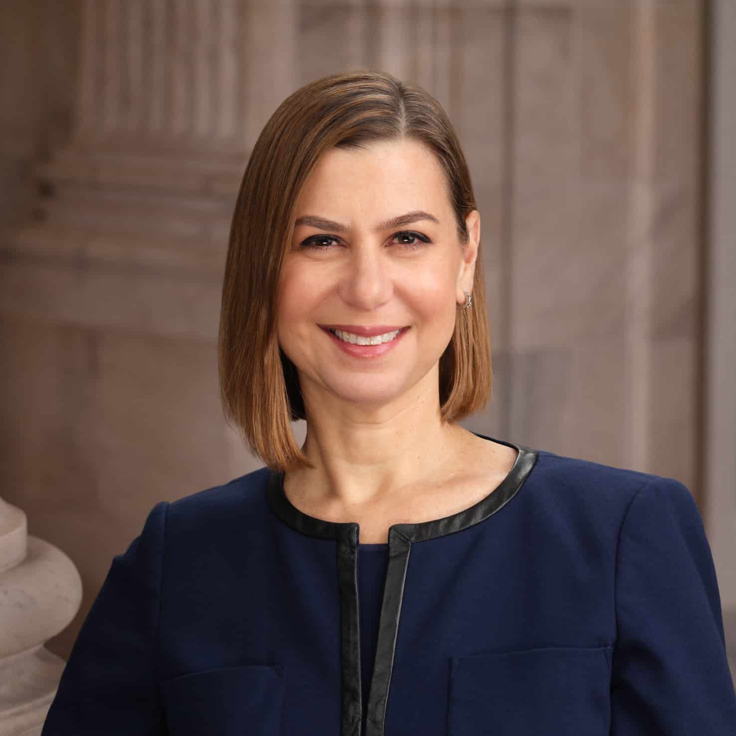 slotkin-square Elissa Slotkin Michigan Senator, standing against a column, smiling, hands held in front in a dark blue suit